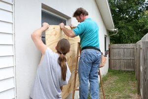 A father and son working together to install plywood over windows in preparation for a hurricane.